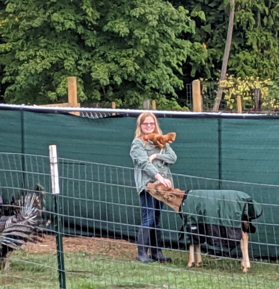 Isabella holding a chicken with a dog beside her